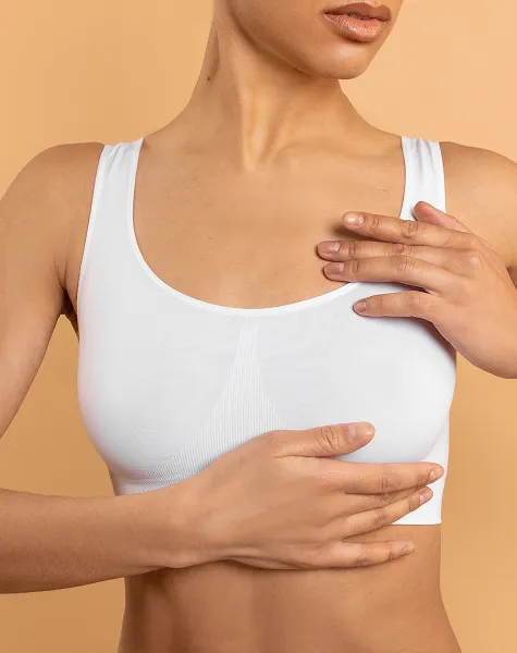Mulher com um top desportivo branco, com as mãos sobre o peito.