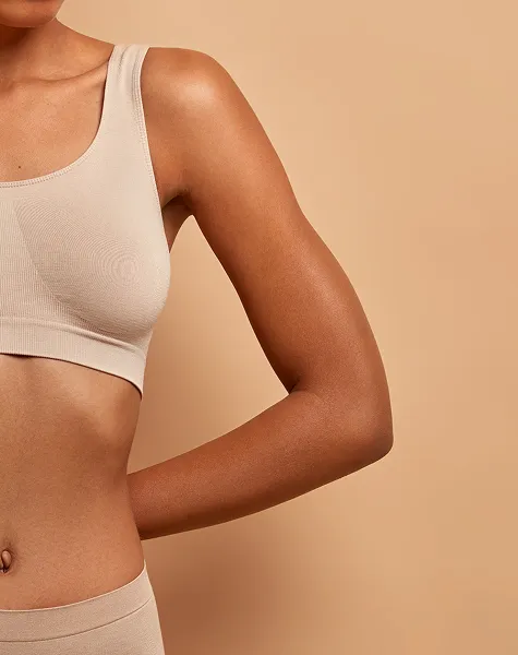 Grande plano do braço e da parte lateral do tronco de uma mulher com um top bege.