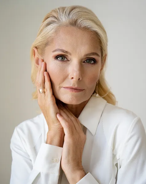 Rosto de uma mulher loira, de camisa branca, com as mãos na bochecha.