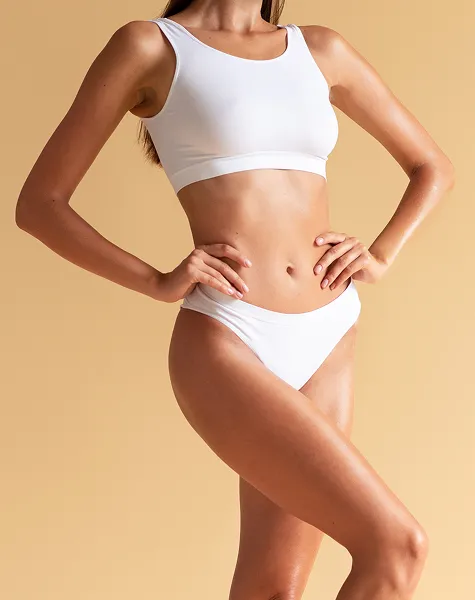 Mulher de frente, a mostrar a barriga e a cintura definidas, com um top e cuecas brancas.