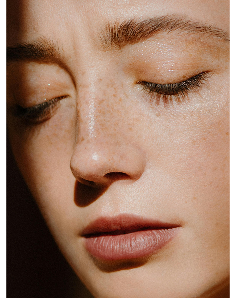 Close-up do rosto de uma mulher com pele saudável e sardas, representando os cuidados da especialidade de dermatologia.