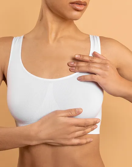 Close-up de uma mulher a tocar no peito com um top desportivo branco