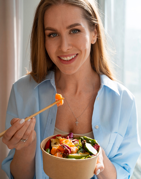 Mulher sorridente a comer uma salada saudável, representando os benefícios de um plano de nutrição personalizado.