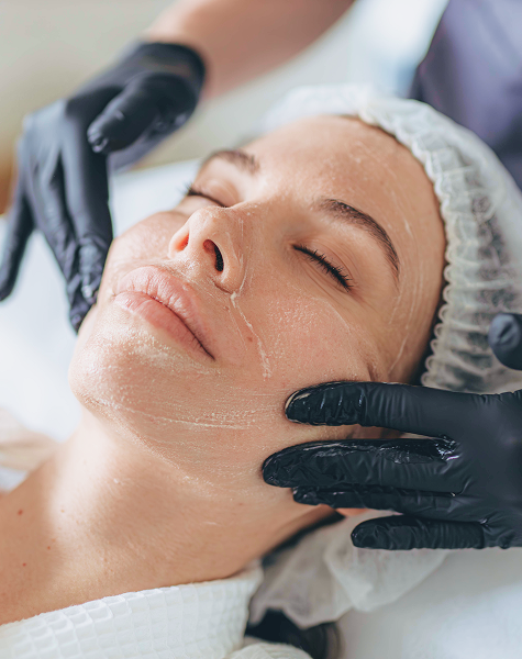 Mulher a receber a aplicação de um produto no rosto por um profissional, durante um procedimento de peeling químico.