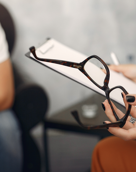 Close-up das mãos de uma psicóloga a segurar uns óculos e uma prancheta, simbolizando uma consulta de psiquiatria.