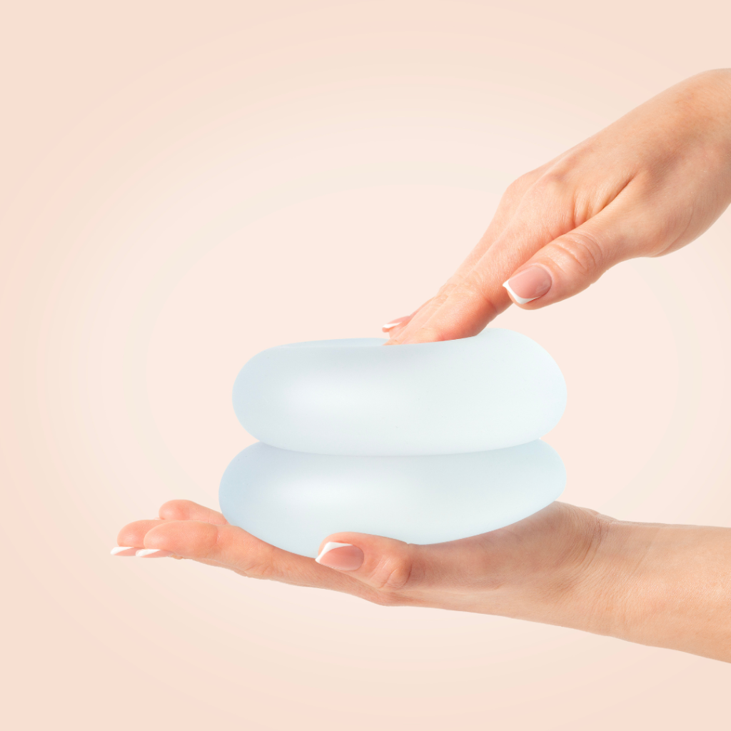 Mãos de mulher cuidadas a segurar e pressionar dois implantes mamários